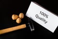 Hammer, three walnuts and paper/note `100% Quality` are on the black table/background. World Quality Day