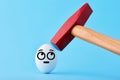 A hammer is about to crush and egg with face with an anxious expression on blue background Royalty Free Stock Photo
