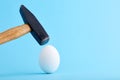 A hammer is about to crush and egg shell on blue background Royalty Free Stock Photo