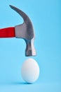 A hammer is about to crush and egg shell on blue background Royalty Free Stock Photo