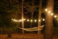 A hammock is strung up between two trees surrounded by cafe lights with starbursts; romantic peaceful evening