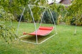 Hammock swing in metal frame with nobody on green lawn in backyard near house cottage. Rest relax relaxation alone on Red hammock