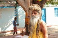 An elderly Holy man with dreadlocked hair walks past a temple in India. Baba.