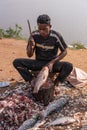 Man hacks tail off fish on shore of Kamalapura Lake, Hampi, Karnataka, India