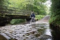 Man riding a mountain bike through a stream ford in a woodland with water splashing