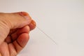 Hand of an acupuncturist holding a long thin acupuncture needle. Man`s hand and metal needle