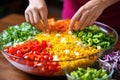hand adding bell peppers to colorful pasta salad