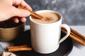 hand adding a cinnamon stick to a mug of latte