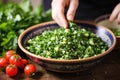 hand adding fresh mint leaves to a bowl of tabbouleh salad