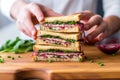 hand adding red onion slices to a stacked sandwich