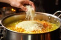 hand adding rice into simmering soup in a stainless steel pot