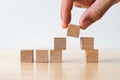 Hand adding wooden cube to unfinished pyramid, symbolizing building, growth, strategy, or progress on light wooden surface with Royalty Free Stock Photo