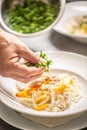 Hand ading fresh parsley to a mix of noodles and carrots, preparing a chicken soup