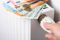 Hand adjusting the valve knob of heating room radiator temperature thermostat with stack of euro money banknotes and coins on it Royalty Free Stock Photo