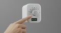 A hand adjusts a white, cube-shaped dial thermostat mounted on a wall. The dial, Royalty Free Stock Photo