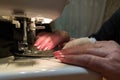 A hand of aged womans with a bandaged finger sews with a sewing machine Royalty Free Stock Photo