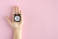 Hand with analog alarm clock composition on pink background