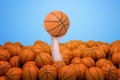Hand appearing out of heap of orange basketball balls holding one on blue background