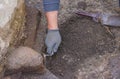 The hand of an archaeologist working on the stratum with a trowel in hand and a charcoal pile on the ground. Work tools