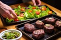 hand arranging grilled venison steaks over a bed of salad