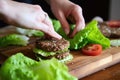 hand arranging lettuce on a beef burger patty