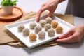 hand arranging sesame balls on a white square platter