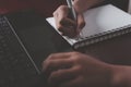 The hand of an Asian girl is using her computer laptop and notebook to study online.