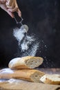 Hand of baker dusting the baguette bread with icing sugar on the dark black background for pastry and bakery concept Royalty Free Stock Photo