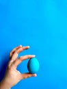 Hand balancing blue egg on a fingertip against solid blue background, minimalist concept for balance, Easter, and