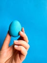 Hand balancing blue egg on a fingertip against solid blue background, minimalist concept for balance, Easter, and
