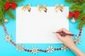 Hand with ballpoint pen over a white blank paper with Christmas border consisting of branches of spruce, christmas toys Royalty Free Stock Photo