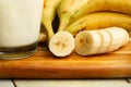 Hand of bananas, a sliced banana and a glass of milk on a wooden kitchen board Royalty Free Stock Photo