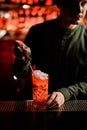 Hand of bartender hold chocolate candy on stick in form of man to decorate glass with cocktail. Royalty Free Stock Photo