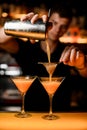 hand of bartender holds shaker with strainer and accurate pours cocktail into martini glass. Royalty Free Stock Photo