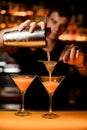 hand of bartender holds shaker with strainer and pours cocktail into martini glass. Royalty Free Stock Photo