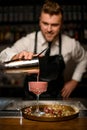 hand of bartender pours cocktail from shaker into crystal glass stands on round tray Royalty Free Stock Photo