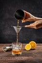 Hand of bartender with shaker and strainer pouring cocktail with brandy and orange bitter