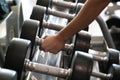 Hand of a beautiful young woman holding a dumbbell from a group of dumbbells lined up in the gym to be used. Healthy mind in a