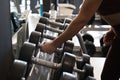 Hand of a beautiful young woman holding a dumbbell from a group of dumbbells lined up in the gym to be used. Healthy mind in a