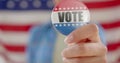Hand of biracial teenage girl agaisnt american flag holding vote badge, slow motion