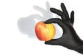 A hand in a black glove holds a red-yellow apple. Shadow on the wall for drama. Isolated on a white background Royalty Free Stock Photo