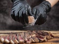 Hand in black glove scratch Himalayan stone salt to sliced beef steak on wooden cutting board. Royalty Free Stock Photo