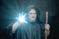 From the hand of a black-hooded monk with a staff, there is a glow on a dark background, a gloomy expression, a medium plan, witch Royalty Free Stock Photo