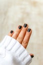 Hand with black manicure on short nails in a white sweater on a light background. The concept of a stylish and warm winter Royalty Free Stock Photo