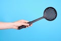 Hand with black plastick ladle utensil. Isolated on blue background