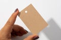 Hand with blank rectangular cardboard label tag for clothes with tiny hole in upper part in center with shadows falling
