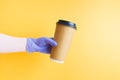 hand in a blue disposable rubber glove holds a shiny gold disposable cardboard cup of coffee for fast food