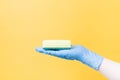 a hand in a blue disposable rubber glove holds a yellow paralon sponge on his palm, yellow background copy space Royalty Free Stock Photo