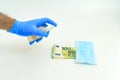 A hand in a blue glove handles with an antiseptic a banknote of money one hundred and 100 euros, next to a blue medical mask. The