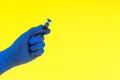 Hand in a blue glove holding medical vial on yellow background. Royalty Free Stock Photo